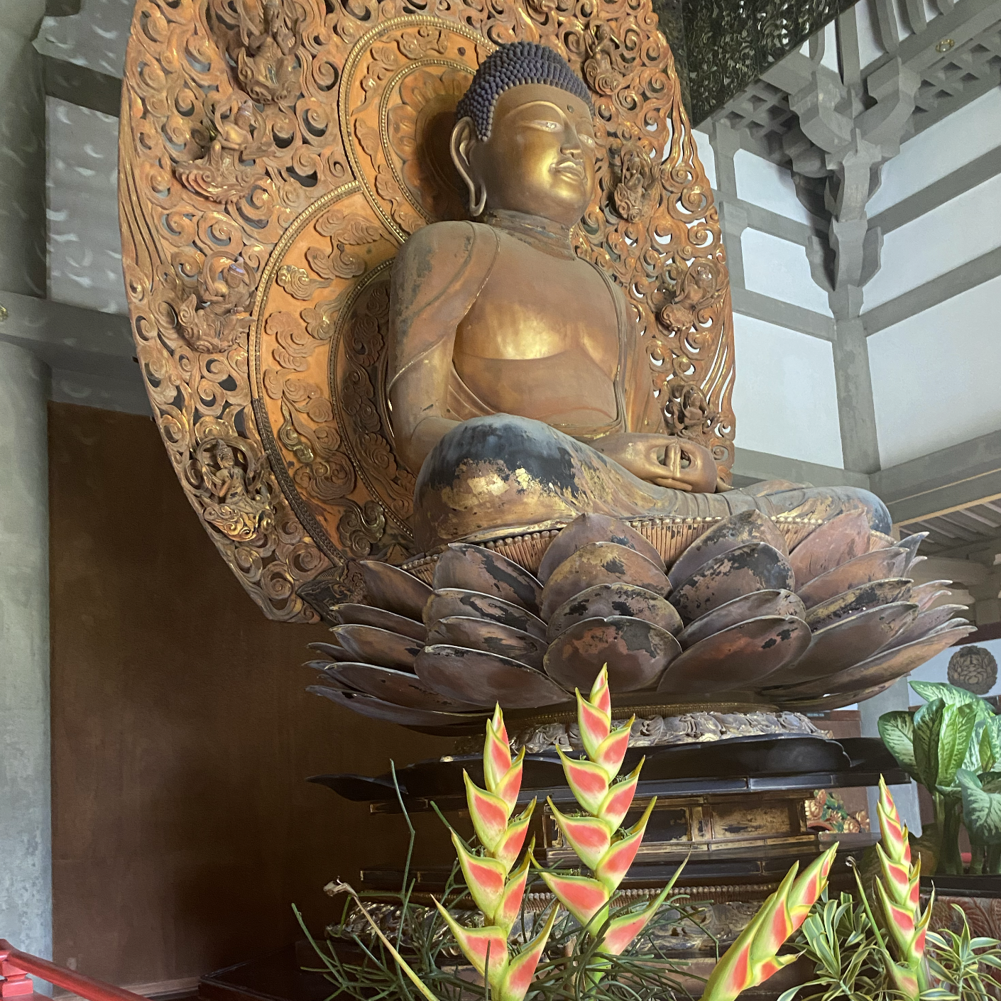 A tall statue of a golden buddha surrounded by tropical flowers and a red rail